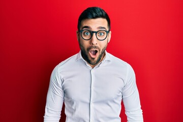 Obraz premium Young hispanic businessman wearing shirt and glasses afraid and shocked with surprise expression, fear and excited face.