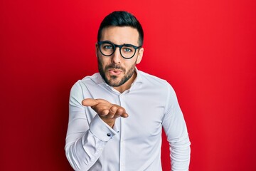 Young hispanic businessman wearing shirt and glasses looking at the camera blowing a kiss with hand on air being lovely and sexy. love expression.