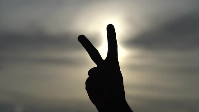 Happy people enjoying nature. Peace two fingers hand sign in front of a sunset in slow motion 