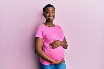 Young african american woman expecting a baby, touching pregnant belly with a happy and cool smile...