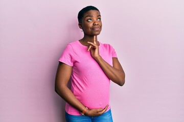 Young african american woman expecting a baby, touching pregnant belly thinking concentrated about doubt with finger on chin and looking up wondering - obrazy, fototapety, plakaty