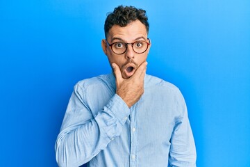 Fototapeta premium Young hispanic man wearing casual clothes and glasses looking fascinated with disbelief, surprise and amazed expression with hands on chin