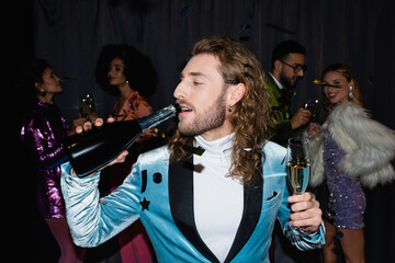 young adult man drinking champagne from bottle on black background.