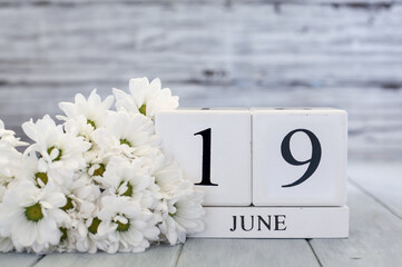 Juneteenth White wood calendar blocks with the date June 19th and white daisies. Selective focus with blurred background. 