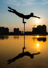 Flexible female circus Artist keep balance and touching the sun against dramatic sunset and cityscape. Motivation, passion and achievement concept 