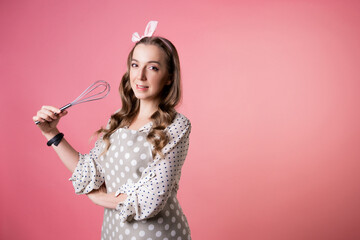 Young charming woman pastry chef with a whisk in her hands. A cook in a polka-dot apron.