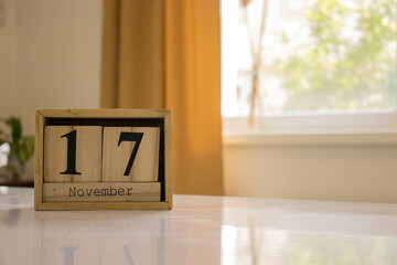 Wooden blocks of the calendar represents the date 17 and the month of November on the background of a window, curtain and a plant.