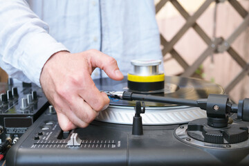 The DJ adjusts the needle on the turntable. Hand of a male DJ in a blue shirt. Unrecognizable young white DJ at the music desk during a DJ set on the terrace of a trendy youth bar.
