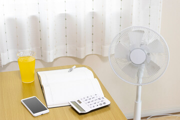 扇風機とノートと電卓。夏に家計簿をつけるイメージ