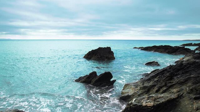 Smooth walk on a Rocky seashore beach with sand and blue water during evening. St Michael's Chapel Of Lammana in Looe, Cornwall, England in 4K. 