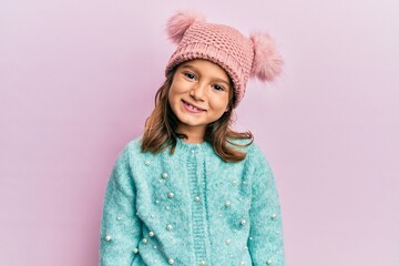 Little beautiful girl wearing wool sweater and cute winter hat with a happy and cool smile on face....