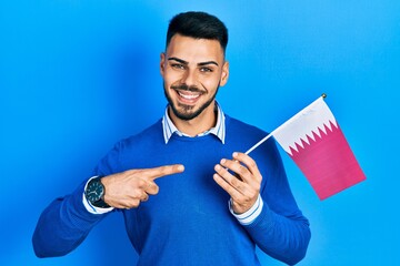 Young hispanic man with beard holding qatar flag smiling happy pointing with hand and finger