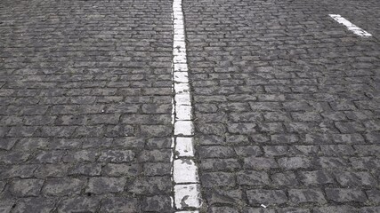 Ancient stone paving road in old town. Cobblestone pavement with damaged white single line road marking in center of frame. Roman road texture background