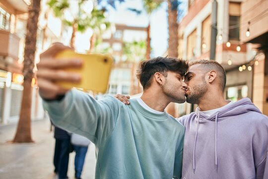 Young gay couple kissing and making selfie by the smartphone at the city.