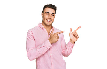 Hispanic young man wearing casual clothes smiling and looking at the camera pointing with two hands and fingers to the side.