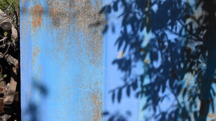 Focus to grunge rusty wall and defocused shadows of tree branches and leaves on grunge wall. Shadow patterns at rusty blue surface of farmhouse