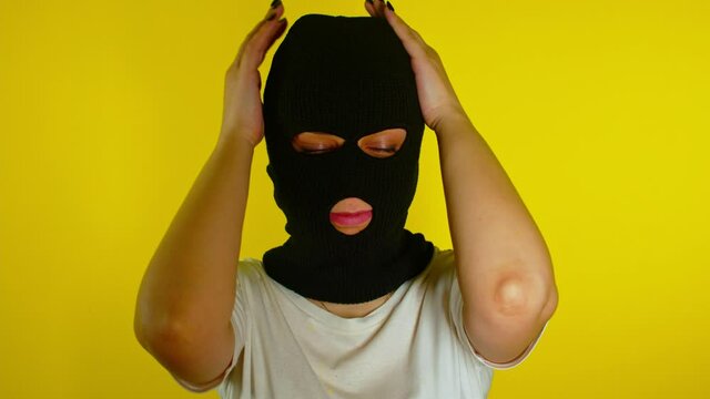 Close up of unrecognizable woman in black balaclava stroking her head and face on yellow background. Unknown person admires soft mask and her image.