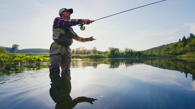 Fly fishing. Amateur angler casts the fly on the calm river at sunset. Fly fisherman casting and fishing on the river