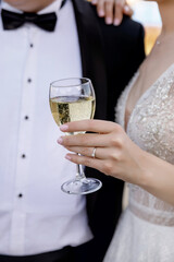 the groom in a black suit with a bow tie and the bride in an exquisite white dress drink champagne