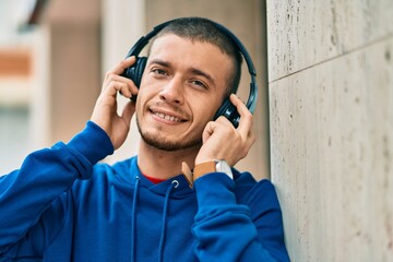 Young hispanic man smiling happy using headphones at the city