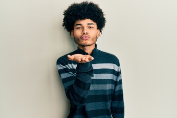 Fototapeta na wymiar Young african american man with afro hair wearing casual clothes looking at the camera blowing a kiss with hand on air being lovely and sexy. love expression.