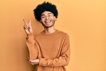 Fototapeta na wymiar Young african american man with afro hair wearing casual winter sweater smiling with happy face winking at the camera doing victory sign. number two.