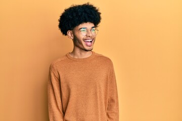 Obraz na płótnie Canvas Young african american man with afro hair wearing casual winter sweater winking looking at the camera with sexy expression, cheerful and happy face.