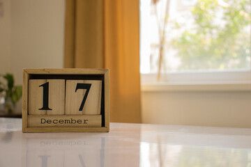 Wooden blocks of the calendar represents the date 17 and the month of December on the background of a window, curtain and a plant