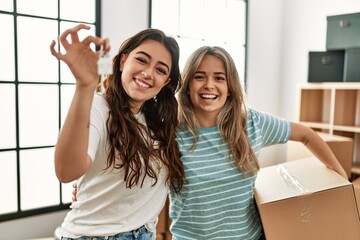 Young beautiful couple smiling happy holding cardboard box and key of new home.
