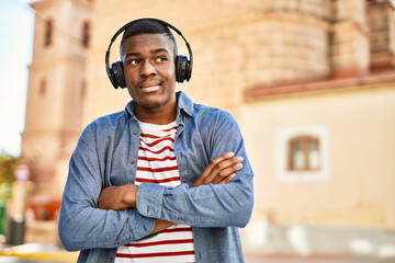 Young african american man with arms crossed gesture using headphones at the city.