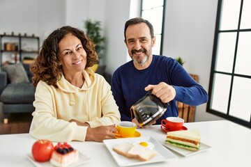Middle age hispanic couple smiling happy sitting on the table having breakfast at home.