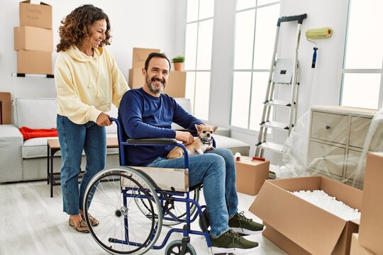 Middle age hispanic couple smiling happy. Man sitting on wheelchair with dog on his legs at new home.
