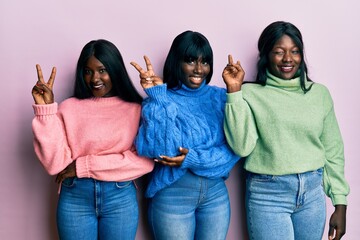 Three young african american friends wearing wool winter sweater smiling with happy face winking at...