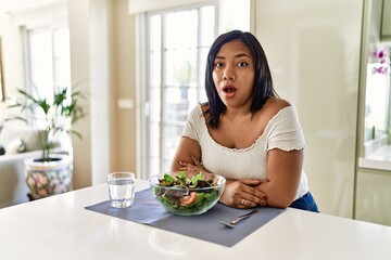Obraz na płótnie Canvas Young hispanic woman eating healthy salad at home afraid and shocked with surprise expression, fear and excited face.