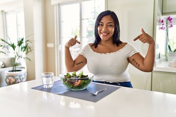 Obraz na płótnie Canvas Young hispanic woman eating healthy salad at home looking confident with smile on face, pointing oneself with fingers proud and happy.