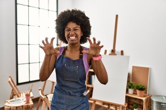 Young african american woman with afro hair at art studio smiling funny doing claw gesture as cat, aggressive and sexy expression