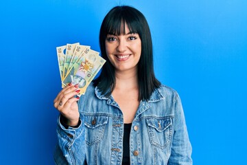 Young hispanic woman holding 50 romanian leu banknotes looking positive and happy standing and...