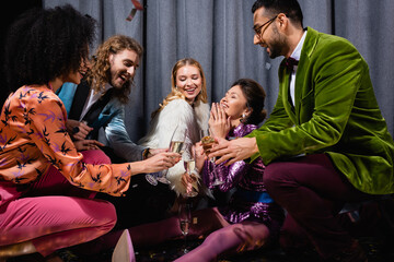 happy asian young adult woman sitting on floor among interracial friends on grey background.