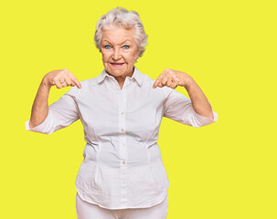 Senior grey-haired woman wearing casual clothes looking confident with smile on face, pointing...