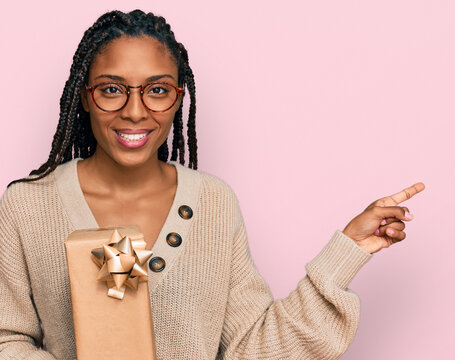 African american woman holding gift smiling happy pointing with hand and finger to the side