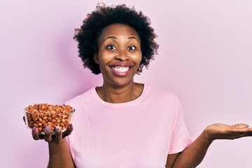 Young african american woman holding peanuts celebrating achievement with happy smile and winner...