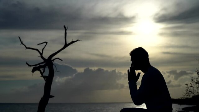 Silhouette of Man pray on sunset and dramatic sky background. Repentance, regret and hope concept 