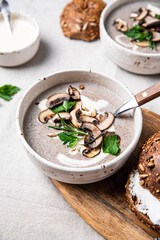 Traditional French mushroom cream soup with sour cream and parsley and rye bun on wooden board on natural linen background .