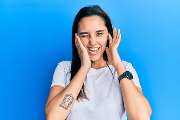 Young hispanic woman wearing casual white t shirt covering ears with fingers with annoyed expression for the noise of loud music. deaf concept.