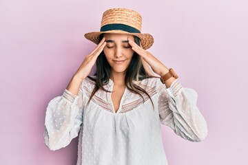 Young hispanic woman wearing summer hat with hand on head, headache because stress. suffering migraine.