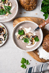 Traditional French mushroom cream soup with sour cream and parsley and rye bun on wooden board on natural linen background .