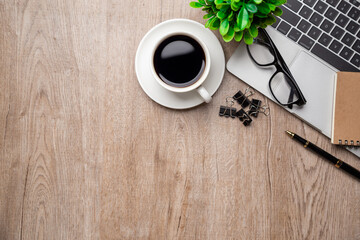 Flat lay, top view office table desk. Workspace with, laptop,office supplies, pencil, green leaf, and coffee cup on wood background.