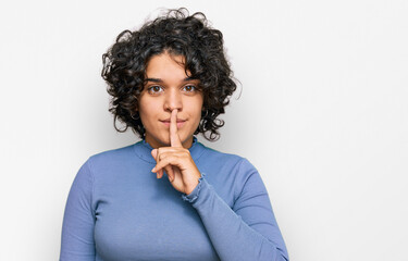 Fototapeta na wymiar Young hispanic woman with curly hair wearing casual clothes asking to be quiet with finger on lips. silence and secret concept.