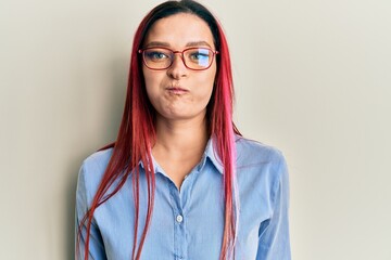 Young caucasian woman wearing casual clothes and glasses puffing cheeks with funny face. mouth inflated with air, crazy expression.