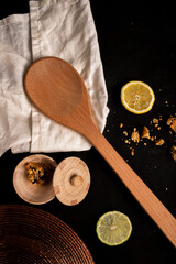 wooden kitchen spoon, white cloth, seasoning pot, lemons, black background